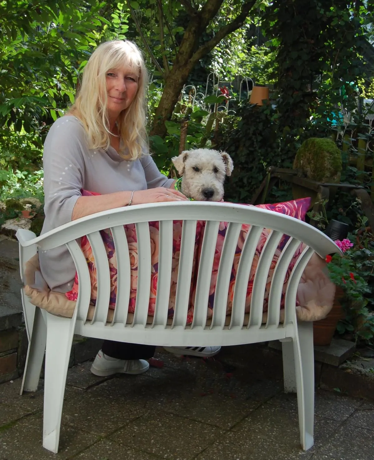 Andrea Hendges-Tiburcy sitzt im Garten auf einer Bank, neben ihr ein kleiner heller Hund